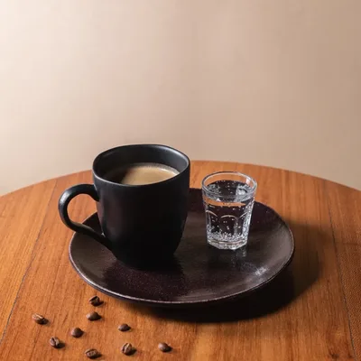 Xícara de café espresso com água ao lado, sobre a mesa de madeira